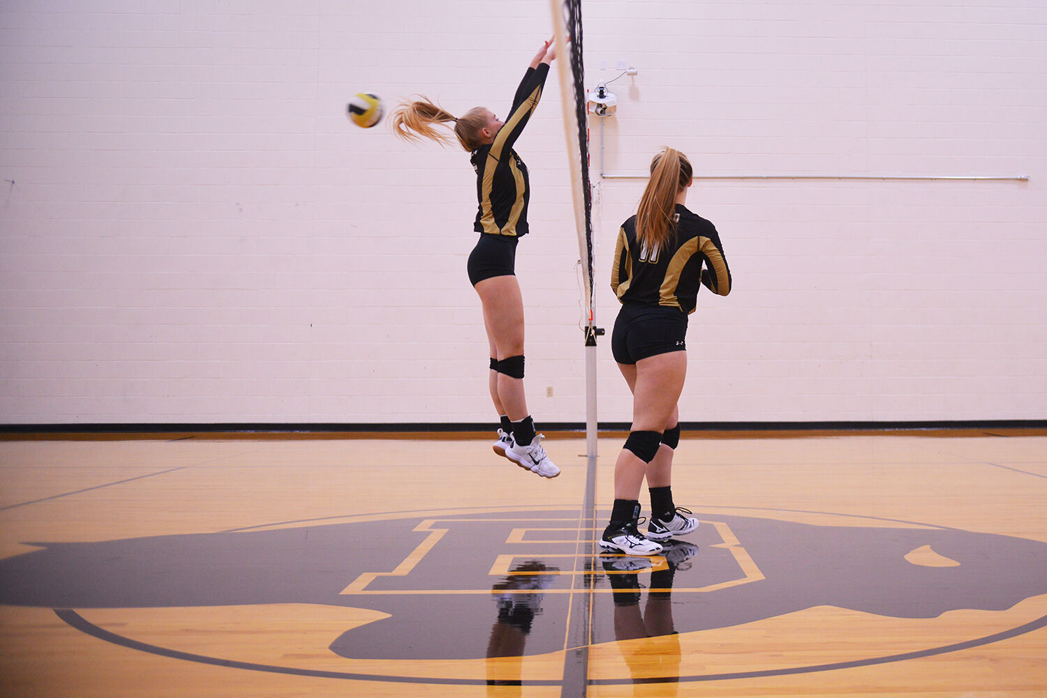 Sydney Downare jumps for a block while setter Cassie Downare watches the hit